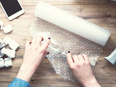 Hands wrapping a stem glass in bubble wrap.